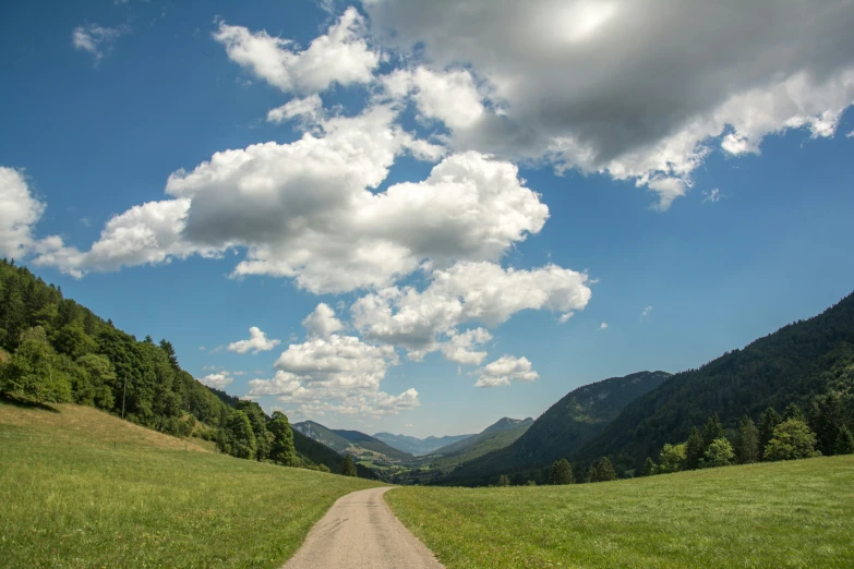 a dirt road leads to a green mountain range