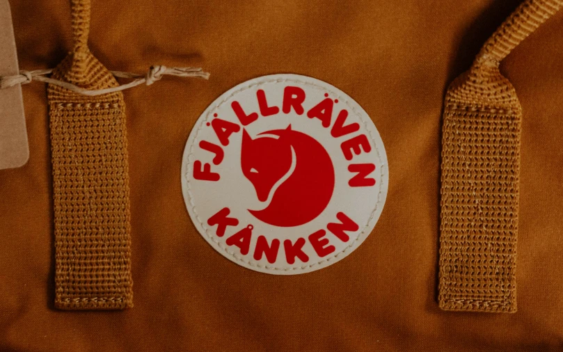 a white sticker reading,'embar avenue tankenn'is on the side of a brown backpack