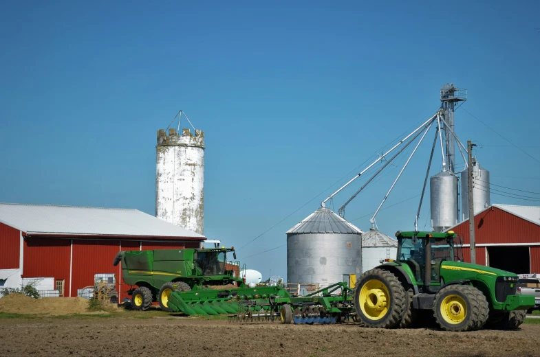 two tractors are parked in the dirt near silos