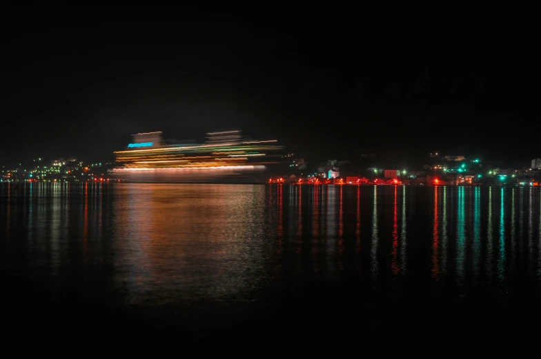 a cruise ship is anchored near a shore line with lights reflected in the water