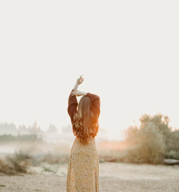 a woman in a yellow dress holds her arms up in the air