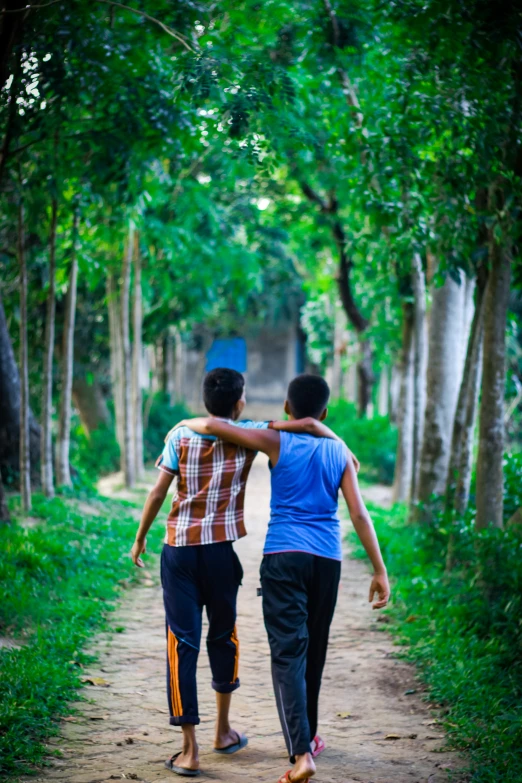 two boys walking down the side of a dirt road in front of trees
