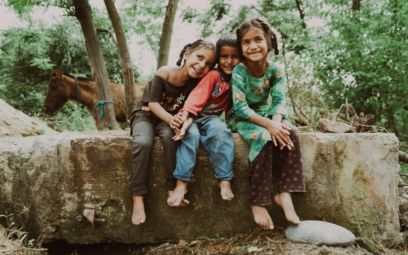 three little girls sitting together on a rock