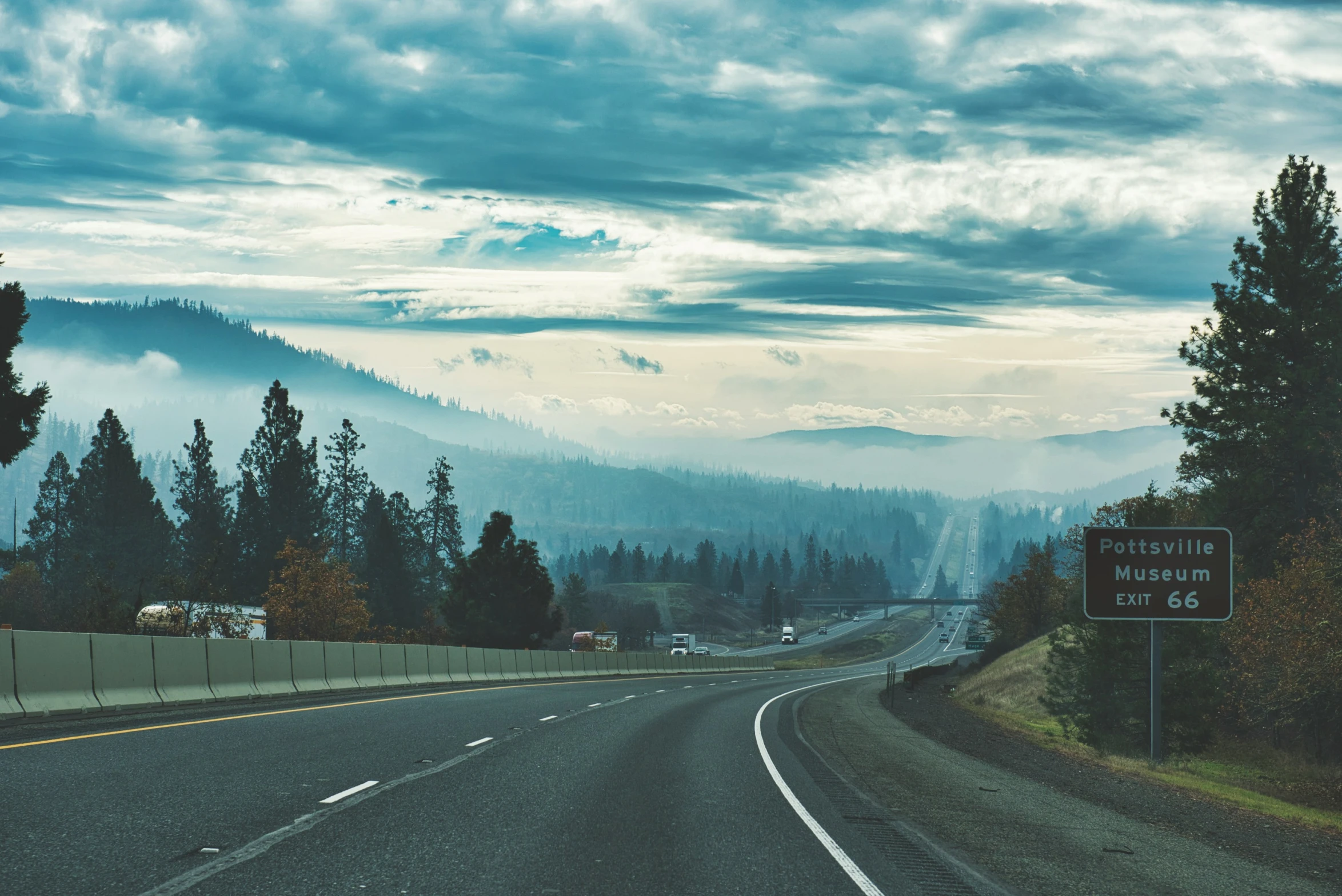 a freeway sign near some trees and hills