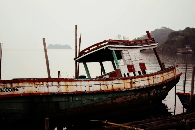 an old, rusted up boat with a wooden pier behind it