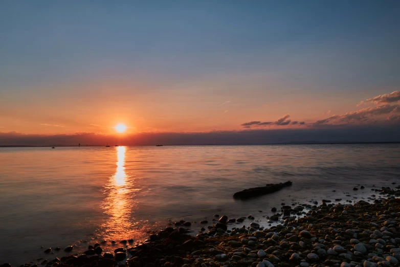 the sun sets over the water off the shore