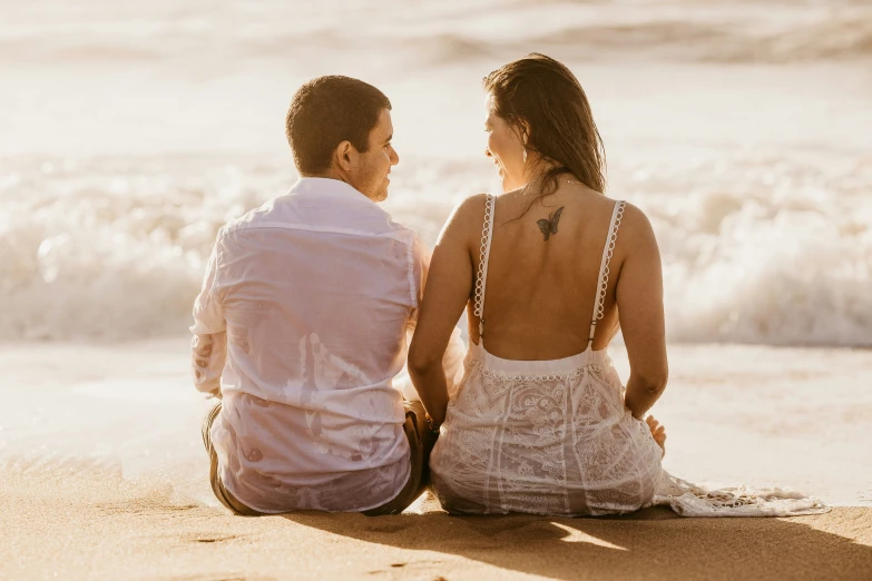 a man and woman sitting on the beach looking out at the water