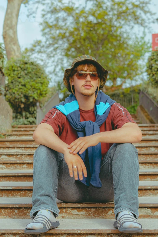 a man sitting on steps wearing sunglasses, a vest and bandana