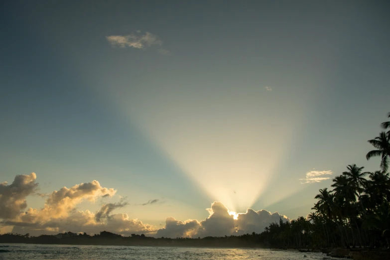 the sun shining through the clouds over a beach