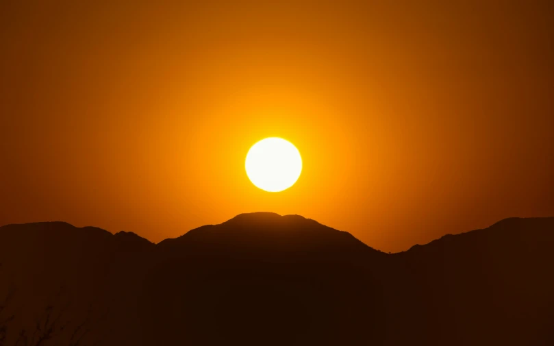 the sun is setting over the mountains near the tree