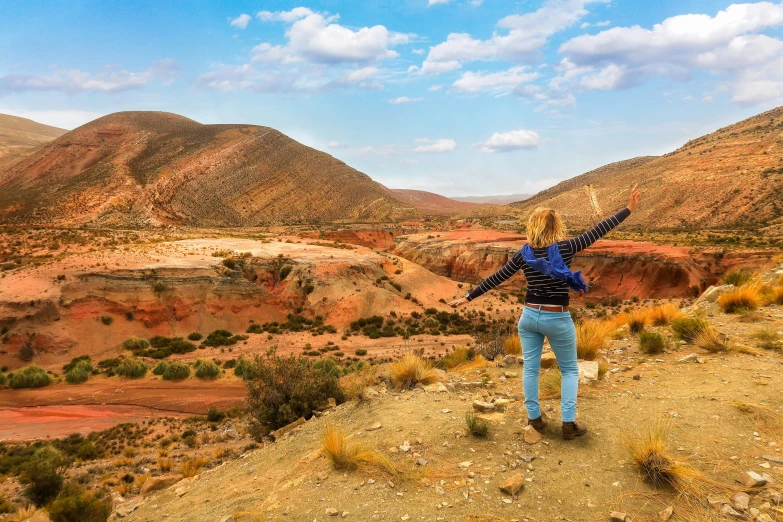 a woman standing on a dirt hill surrounded by mountains