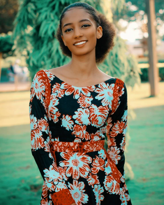 a woman with an afro smiling in a black floral print dress