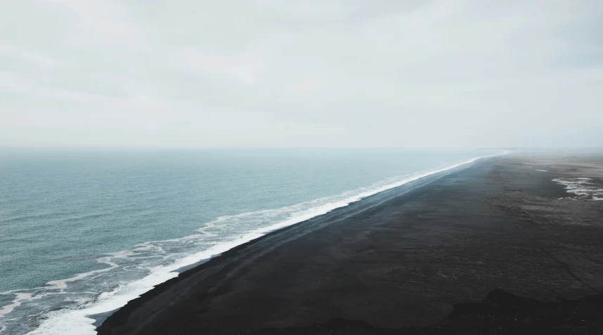 a long black beach with large waves coming in