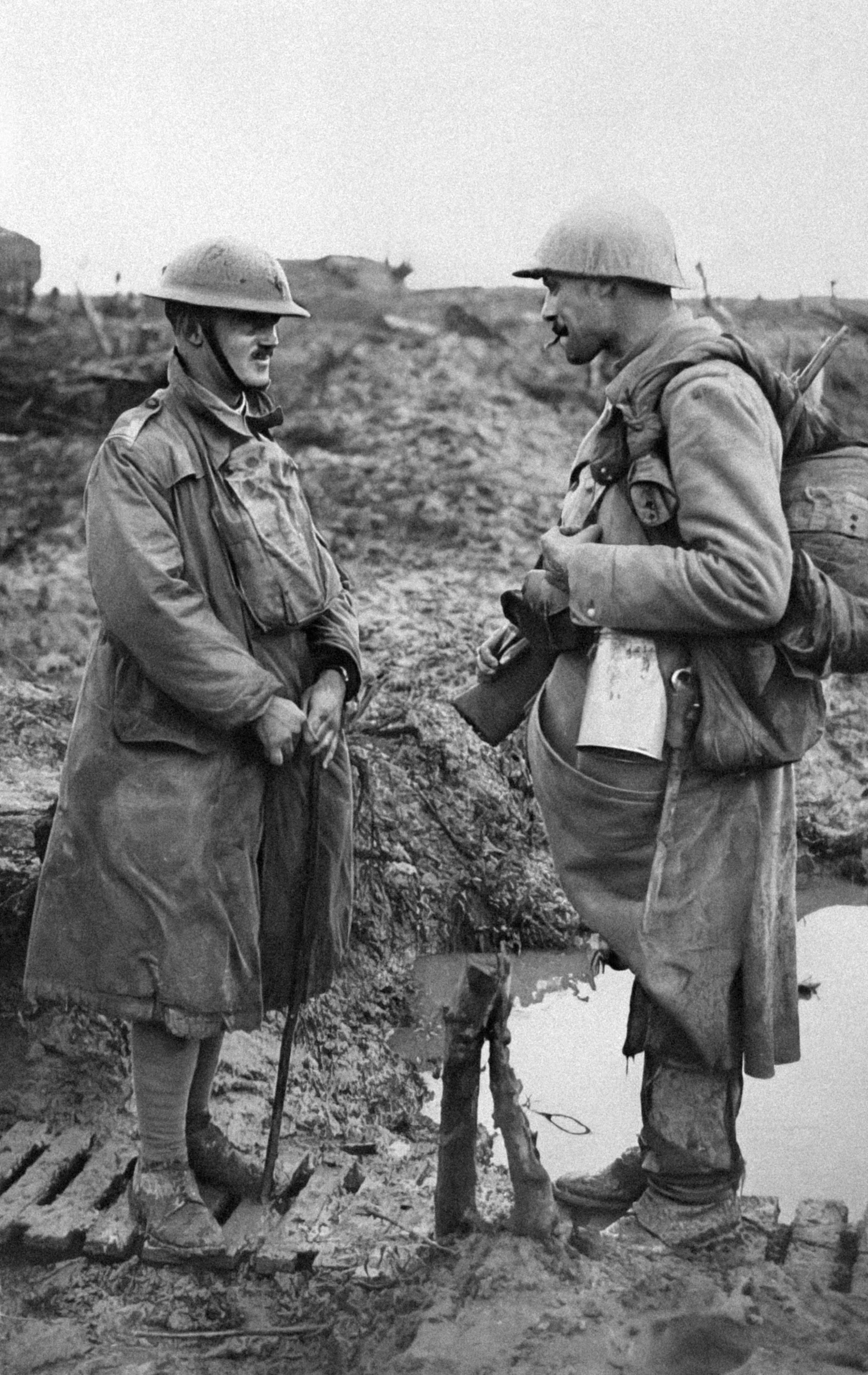 two soldiers stand in the mud talking to one another