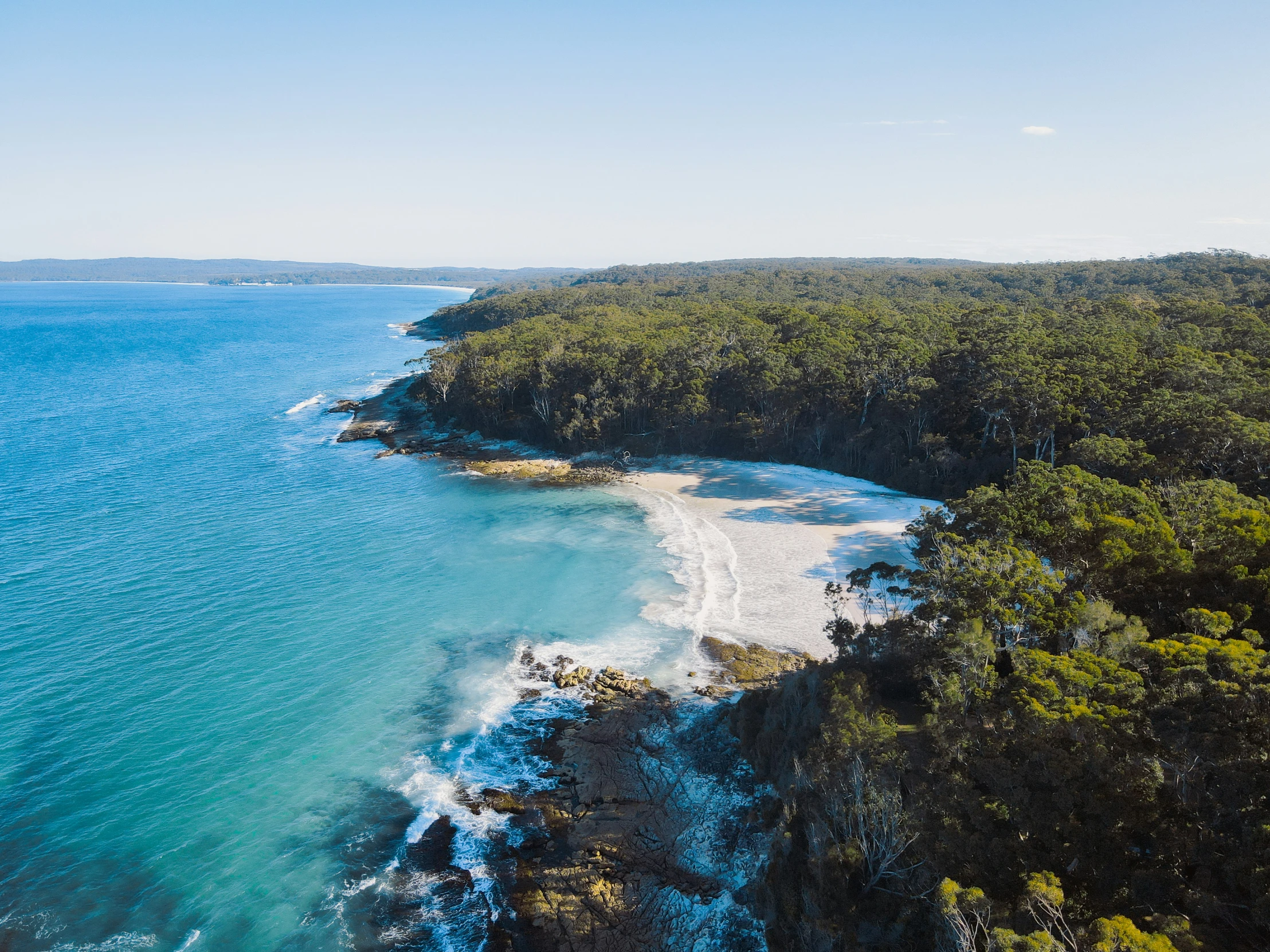 an aerial s of the coastline with water, sand and forest