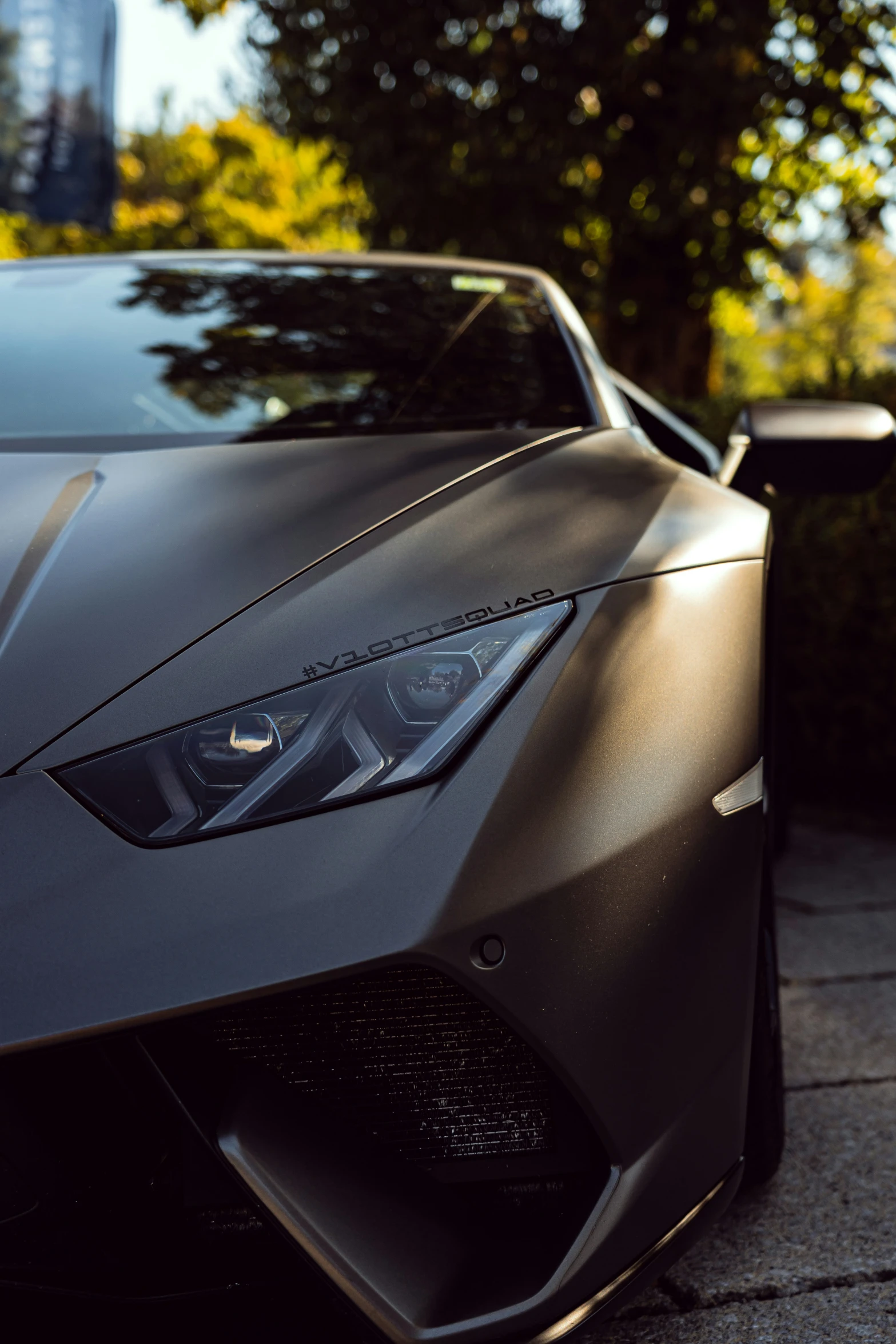 the hood of a silver sports car with its lights on