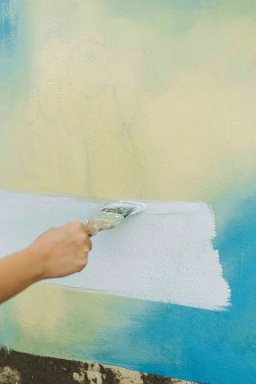 a hand holding a paint brush over a blue and white paint