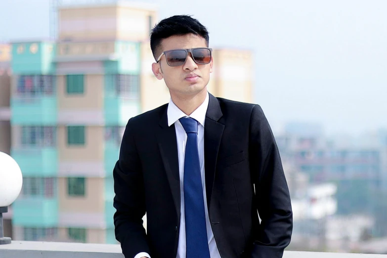 the man wearing sunglasses and a suit is leaning against a wall