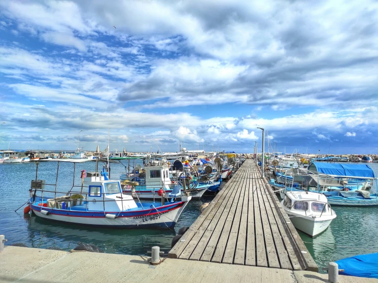 several boats parked on a dock while cloudy skies fly over