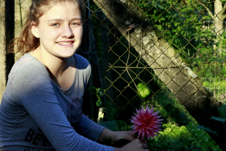 a woman holding a pink flower in front of a chain link fence