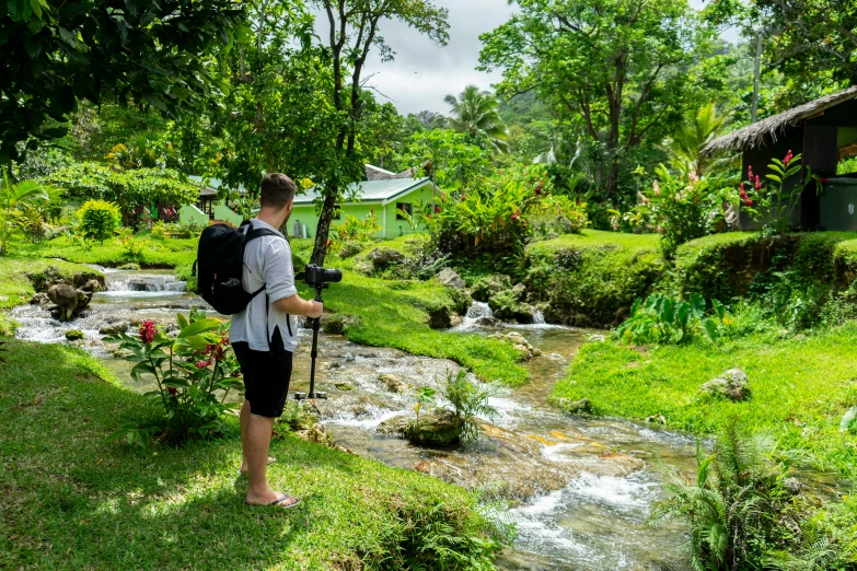 a man wearing a backpack is standing near a stream