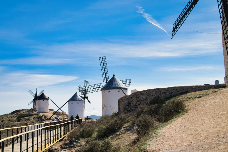 two windmills are located on a hill behind a fence