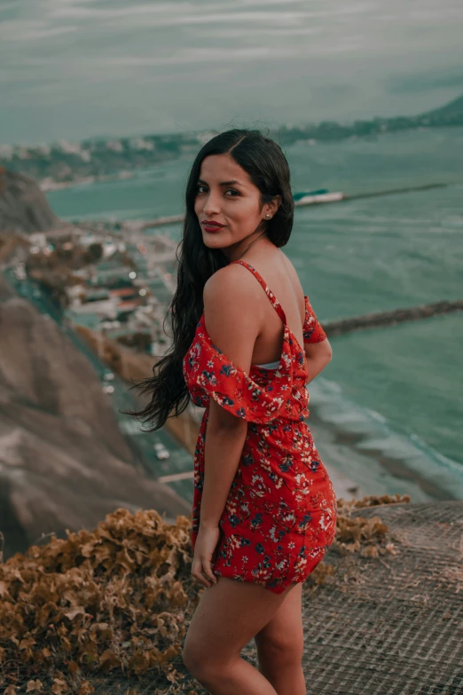 a woman in a red flowered dress standing on the side of a mountain