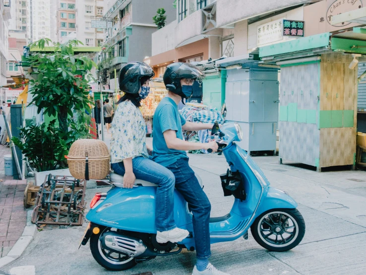 two people on a blue scooter riding on a city street