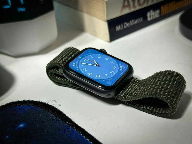 a smart watch with blue face is wrapped in olive green fabric