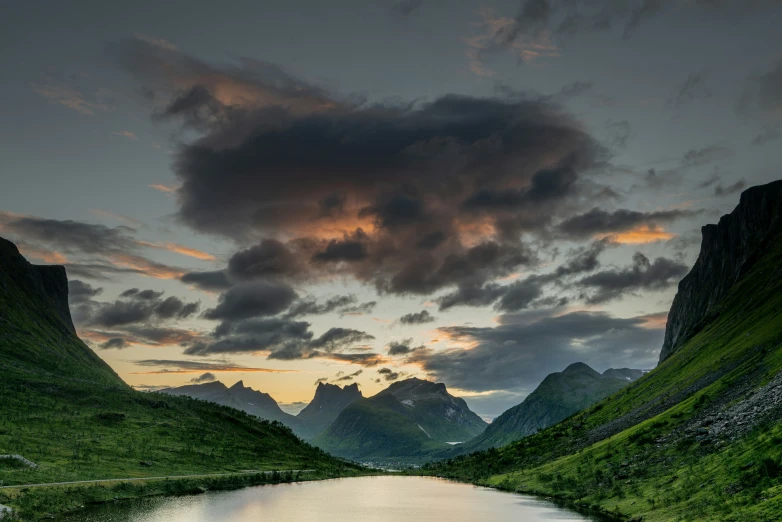 the water has green grass and mountains behind it