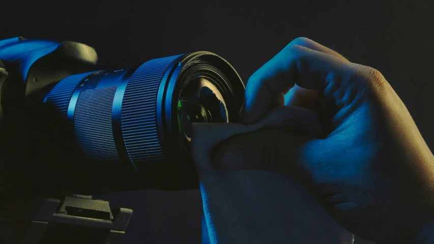 a hand is holding a blue camera in a black room