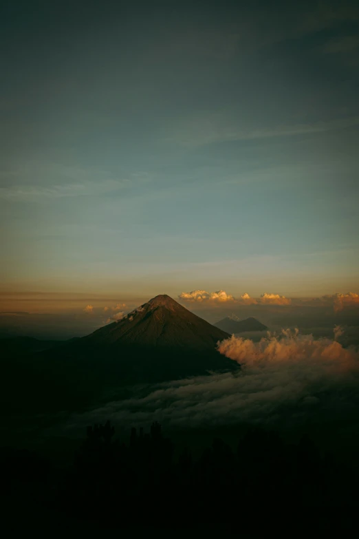 a mountain above clouds at dusk with the sky getting dark