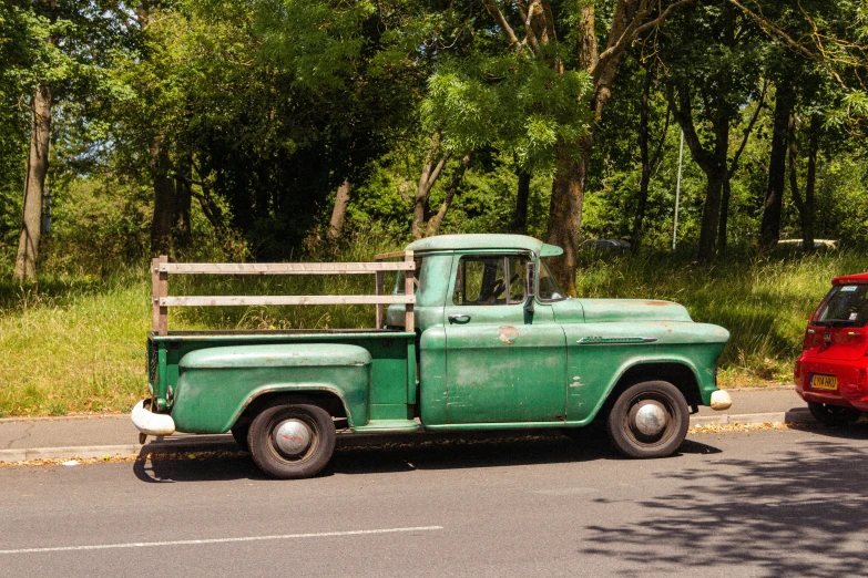 an old green truck parked in front of a red car