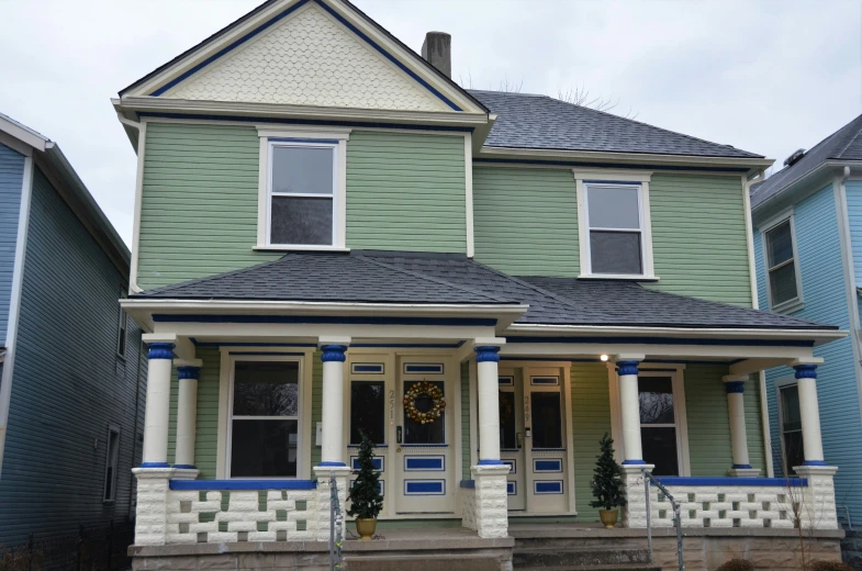 green house with blue trim and pillars and some bushes on the front yard