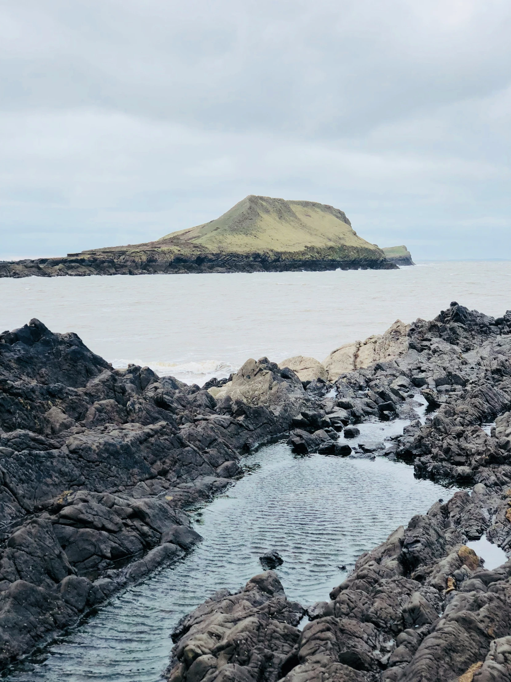 an island sitting behind the ocean as seen from a rocky shore