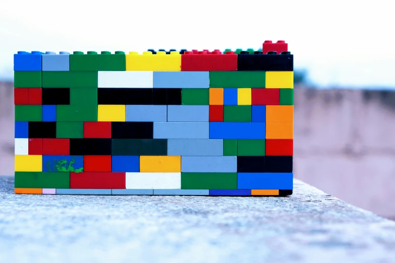 the multi - colored lego blocks sit in front of a gray concrete wall