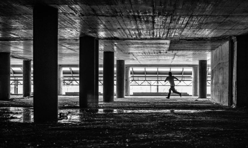 black and white image of man walking underneath an overpass
