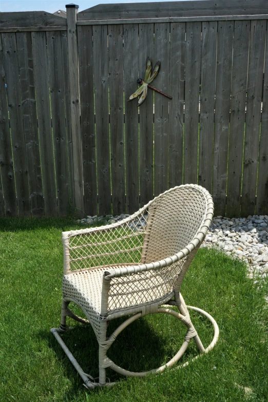 an antique wooden rocking chair in the grass near a fence