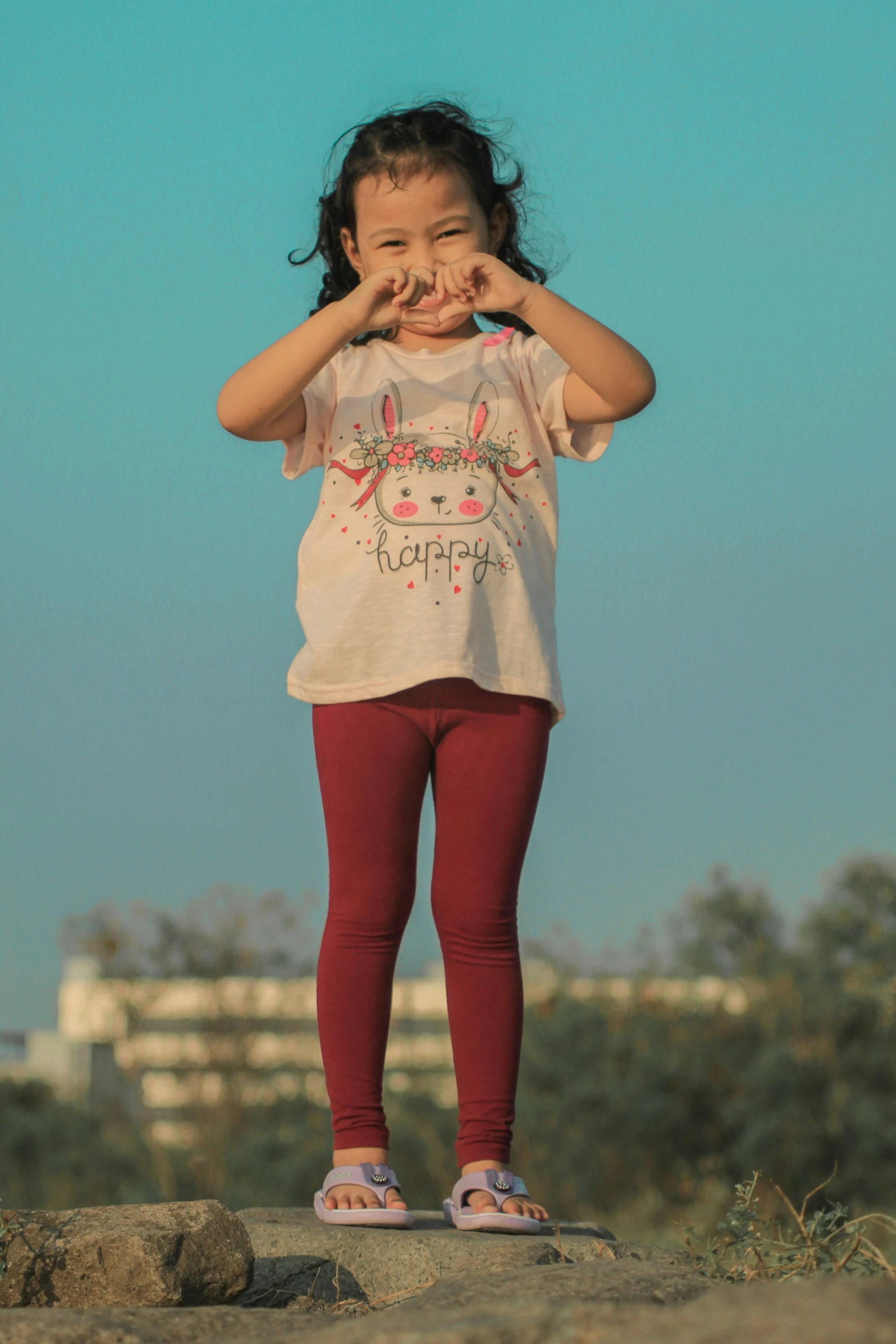 the girl is standing on top of rocks holding her hands out for her face