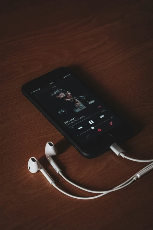 an ipod with earbuds resting on top of a wooden surface