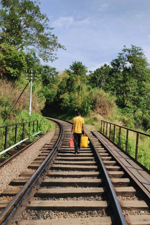 a man walks along a railway track holding two bags