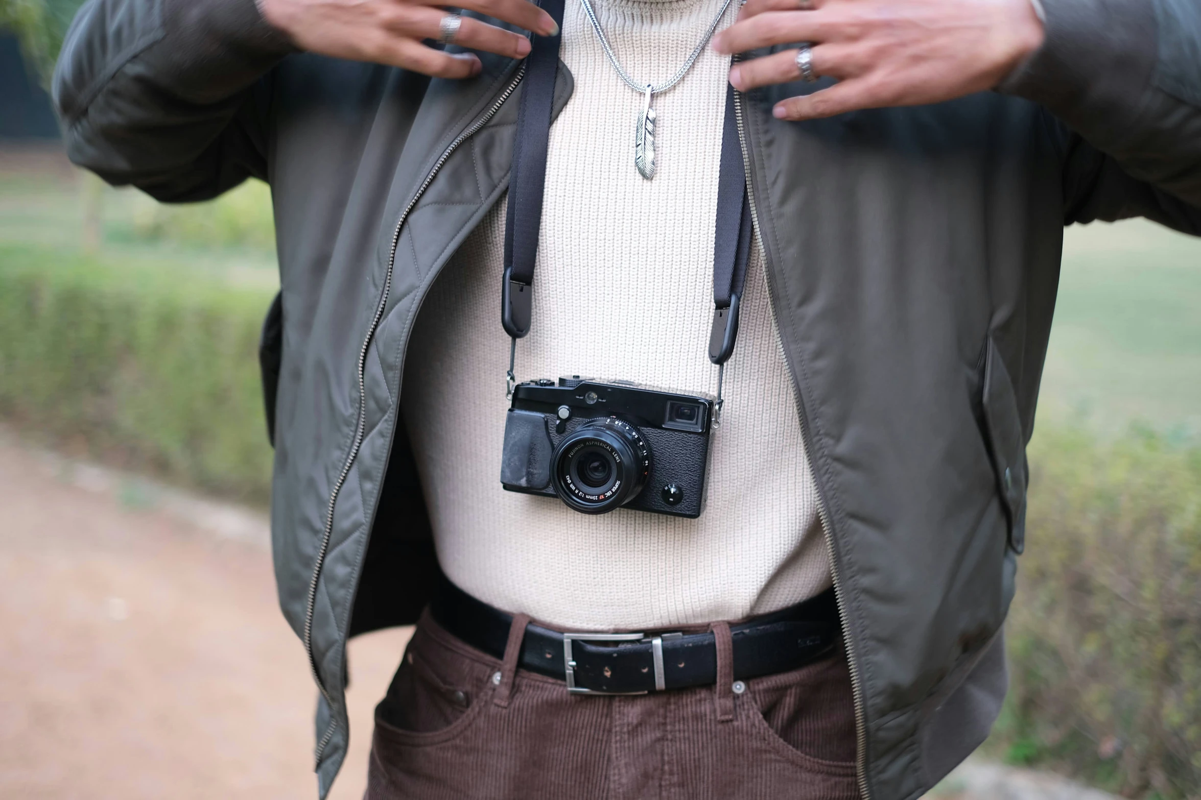 a man in brown pants holding a camera and wearing a necklace