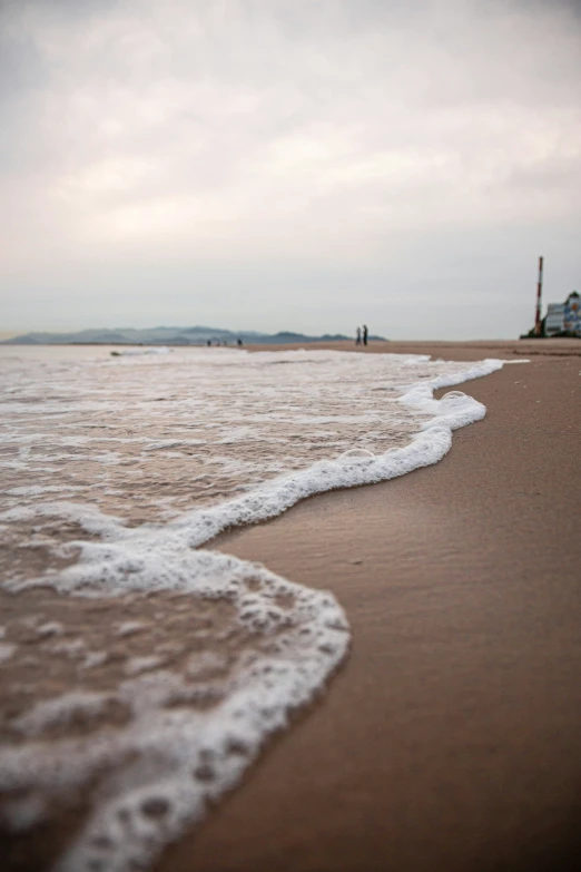 waves in the sand on a beach, with a building in the background