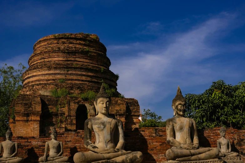 three statues sitting in the foreground near a pagoda with a brick wall behind them