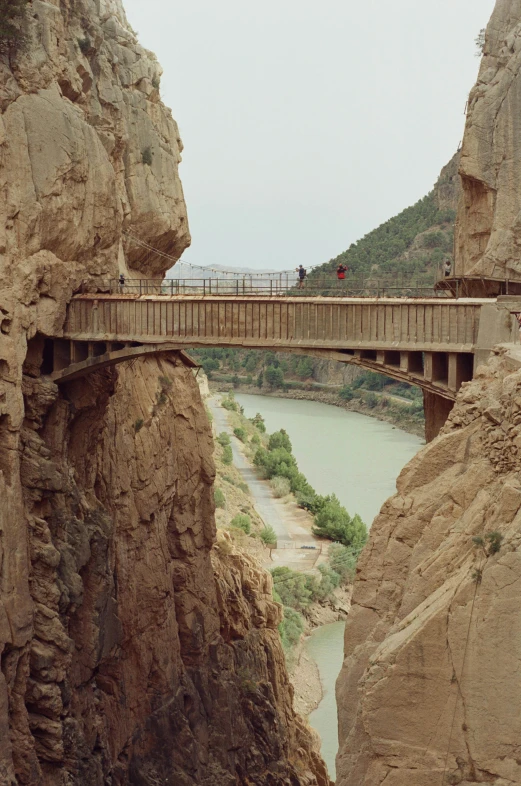 people are walking across a bridge above a mountain stream