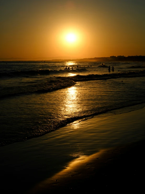 the sun sets over a sandy beach near the water