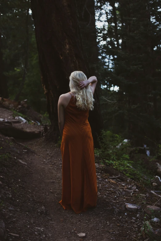 a woman in an orange dress walking in the woods