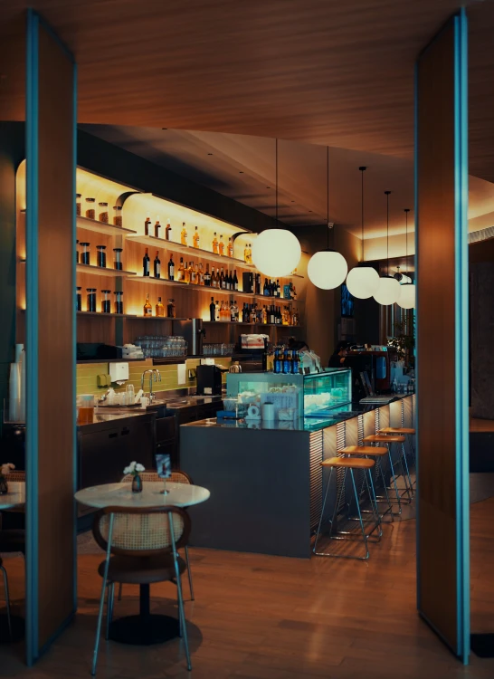 the interior of a restaurant with tables, stools and lights