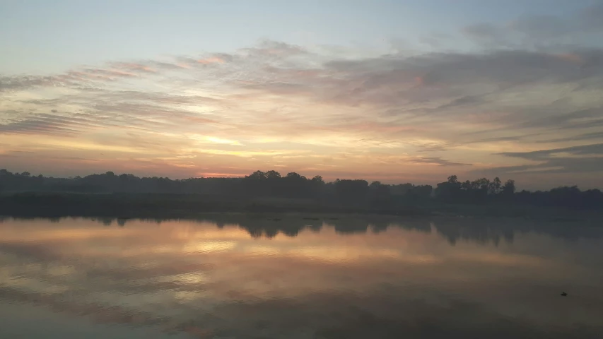 a lake surrounded by forest at sunrise with clouds in the sky