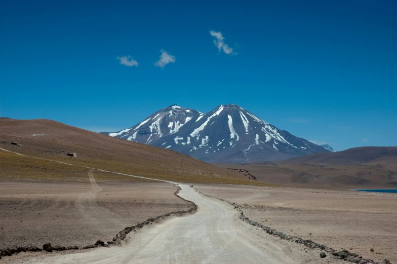 a dirt road runs toward a snow covered mountain